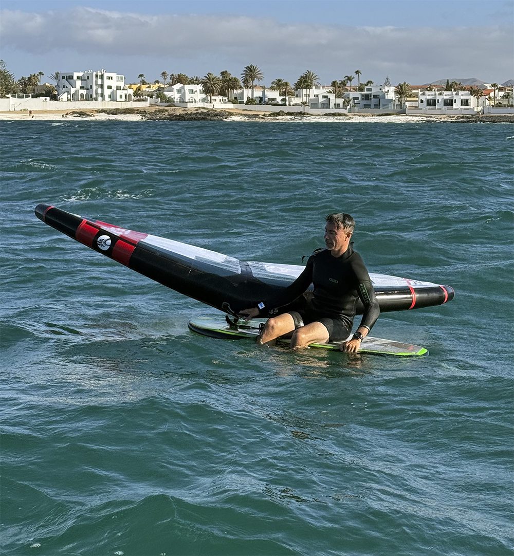Alumno de wing foil sentado en la tabla con el ala en el agua